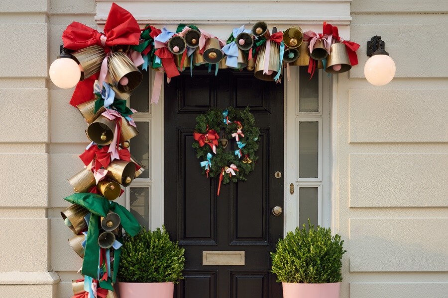 Ytterdörr med en girlang av gyllene klockor och röd‑gröna band upphängd med Command Outdoor‑krokar, samt en krans på en Command‑kranskrok.
